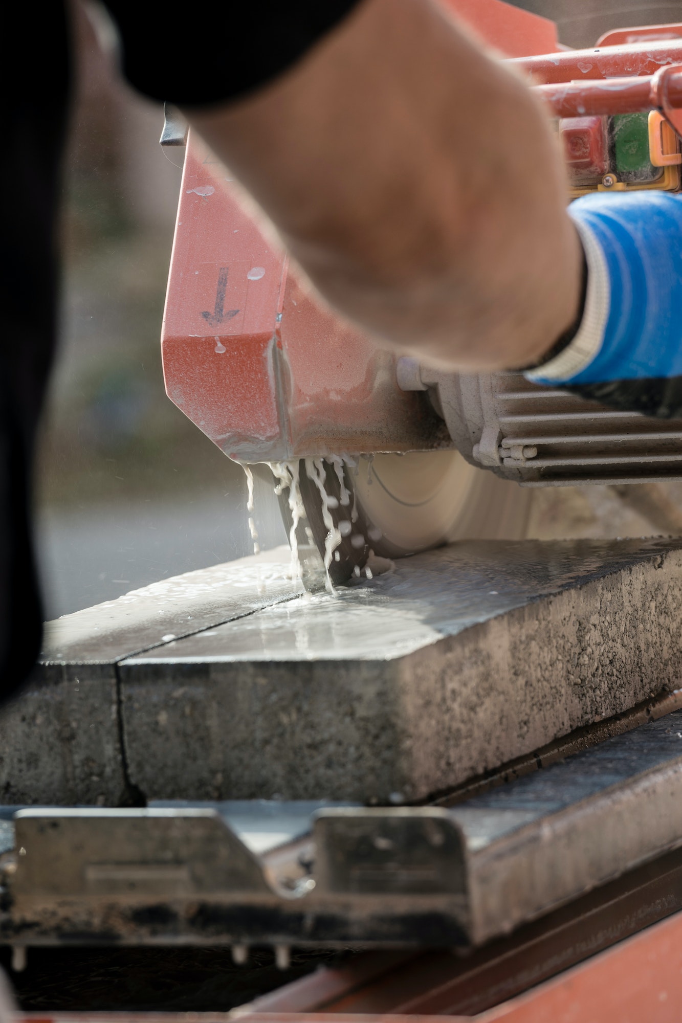 Workman using an angle grinder to cut a concrete block in a rear view